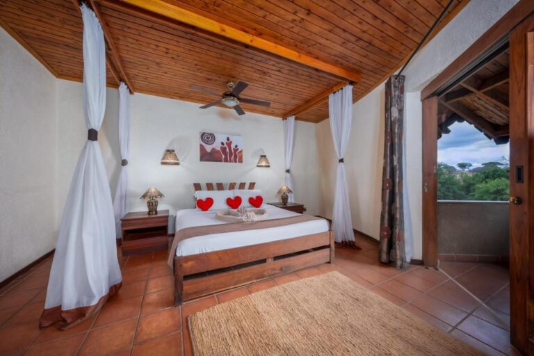 Ein Zimmer mit großem Bett unter einer Holzdecke, mit Vorhängen und Balkon