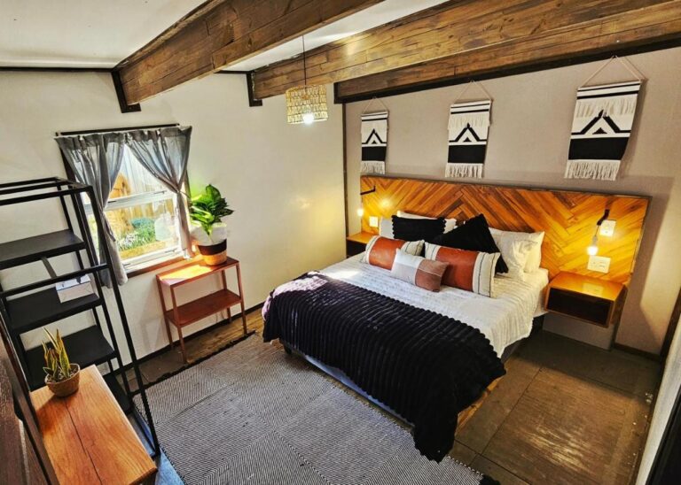 Ein Zimmer im The Elements mit großem Bett, Kopfteil aus Holz im Fischgrätmuster und drei schwarz-weißen Wandbehängen, unter sichtbaren Balken