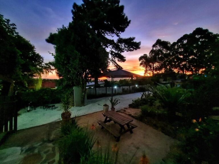 Der Garten bei Sonnenuntergang, mit einem Picknicktisch unter großen Bäumen und orangefarbenem Himmel