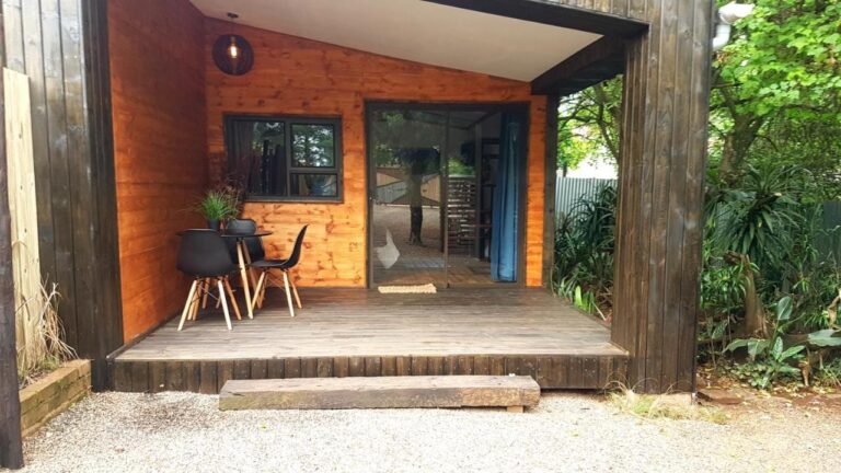 Die Holzterrasse eines Chalets mit Tisch und zwei schwarzen Stühlen vor einer gläsernen Schiebetür