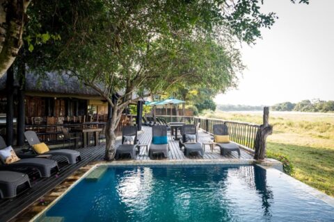 Der Pool der Umkumbe Safari Lodge und ihre Holzterrasse über dem grasbewachsenen Flussufer