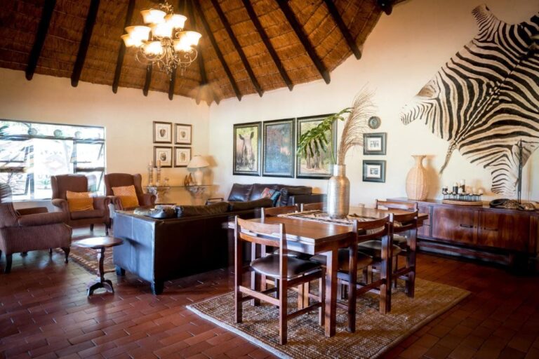 Eine Lounge unter dem Strohdach, mit Ledersofas, Esstisch und einem Zebrafell an der Wand