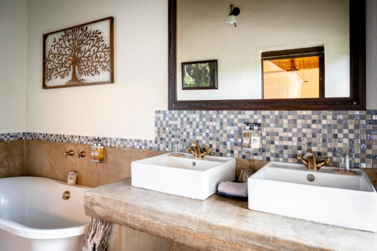 Ein Bad mit zwei Waschbecken auf einer Betonablage, einer Badewanne und einem Fliesenspiegel aus Mosaik