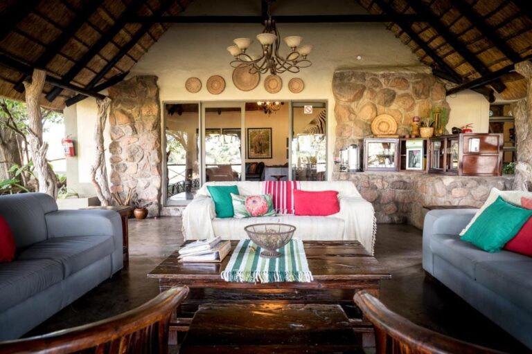 Die offene Lounge der Umkumbe Safari Lodge unter dem Strohdach, mit grauen Sofas und Steinmauern