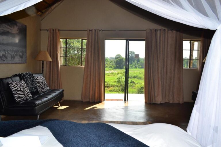 Ein Zimmer, durch eine Glastür offen zum grünen Busch, mit schwarzem Ledersofa und Kissen im Zebramuster