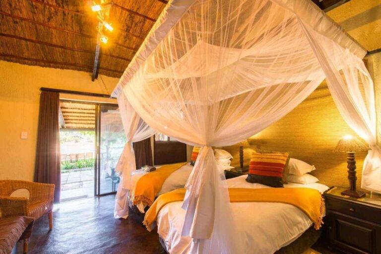 Ein Zimmer mit zwei Betten unter Moskitonetzen, gelben Decken und einer offenen Glastür zur Terrasse