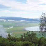 Der grüne Kraterboden vom Rand aus gesehen, mit dem Magadi-See und Wolken an den Kraterwänden